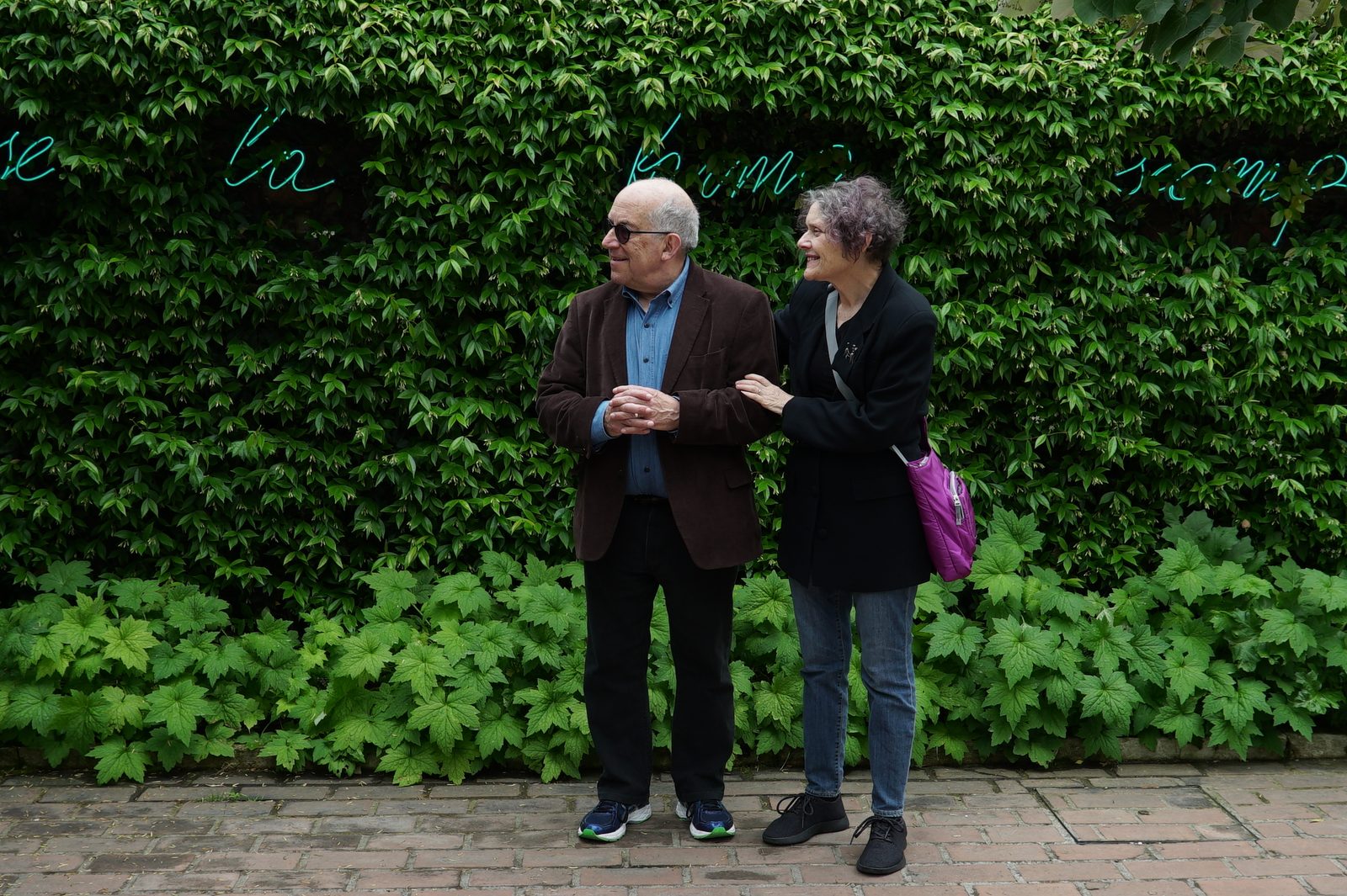 David arm in arm with a woman in front of a wall of green ivy
