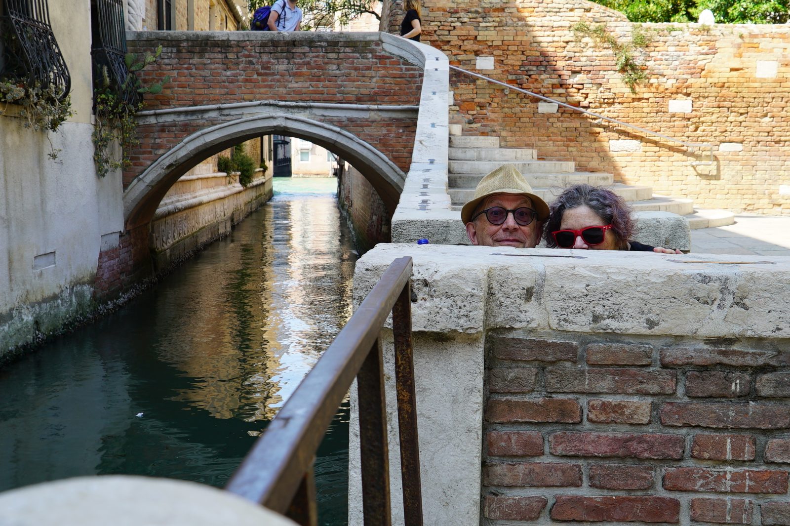 David and a woman peeking over a stone wall next to a small canal
