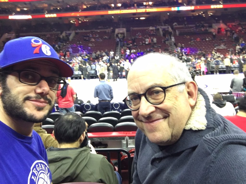 David and a younger man in a 76ers cap at a basketball arena