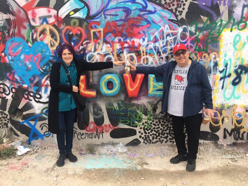 David and a woman reaching toward each other in front of a graffiti wall that reads LOVE