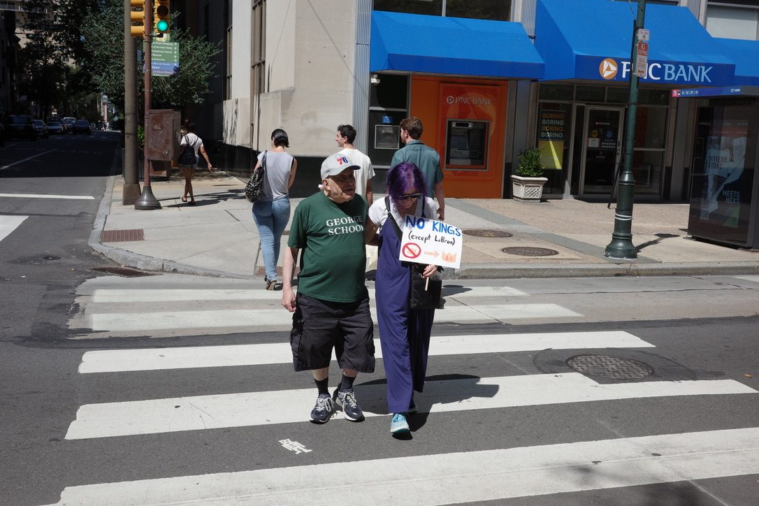 David and a woman crossing a city street, she carries a handmade sign