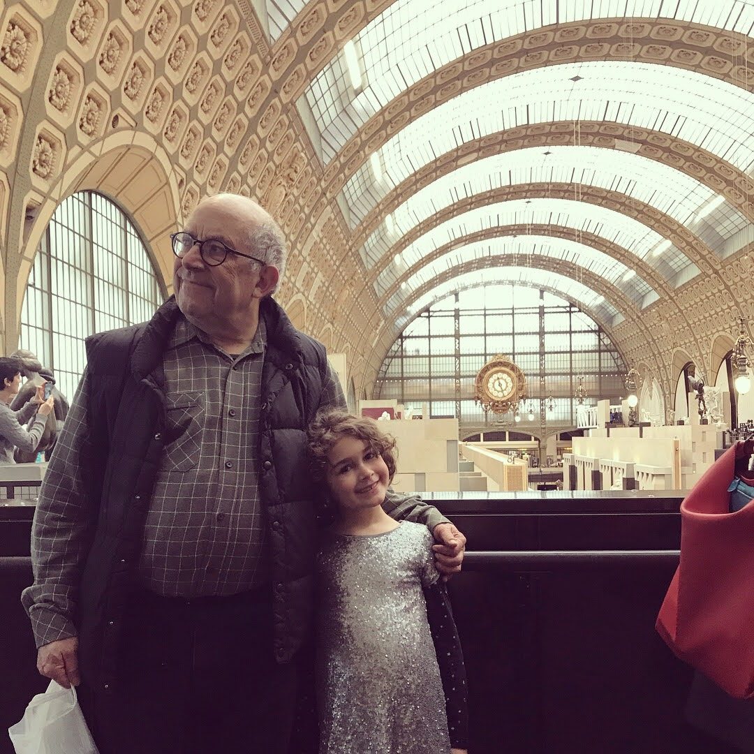 David with his arm around a girl in a grand museum hall with a large clock