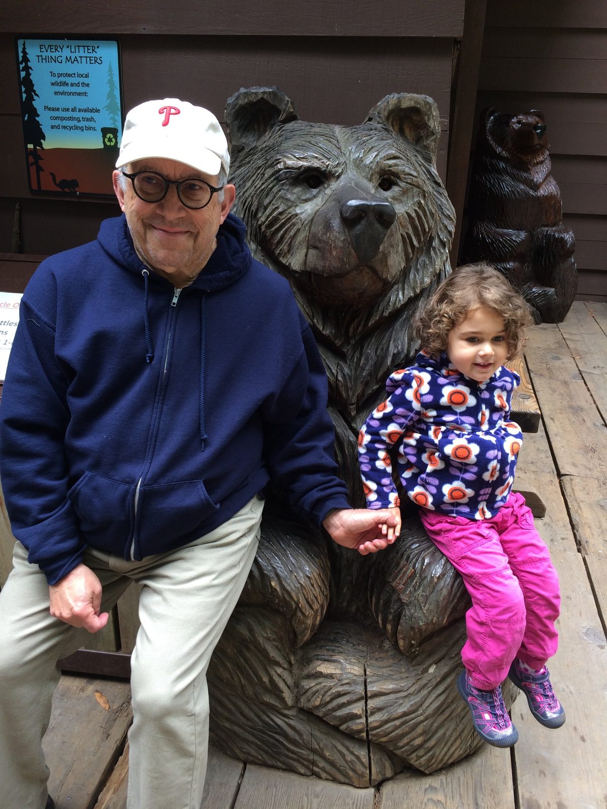David in a Phillies cap holding hands with a young girl beside a carved wooden bear