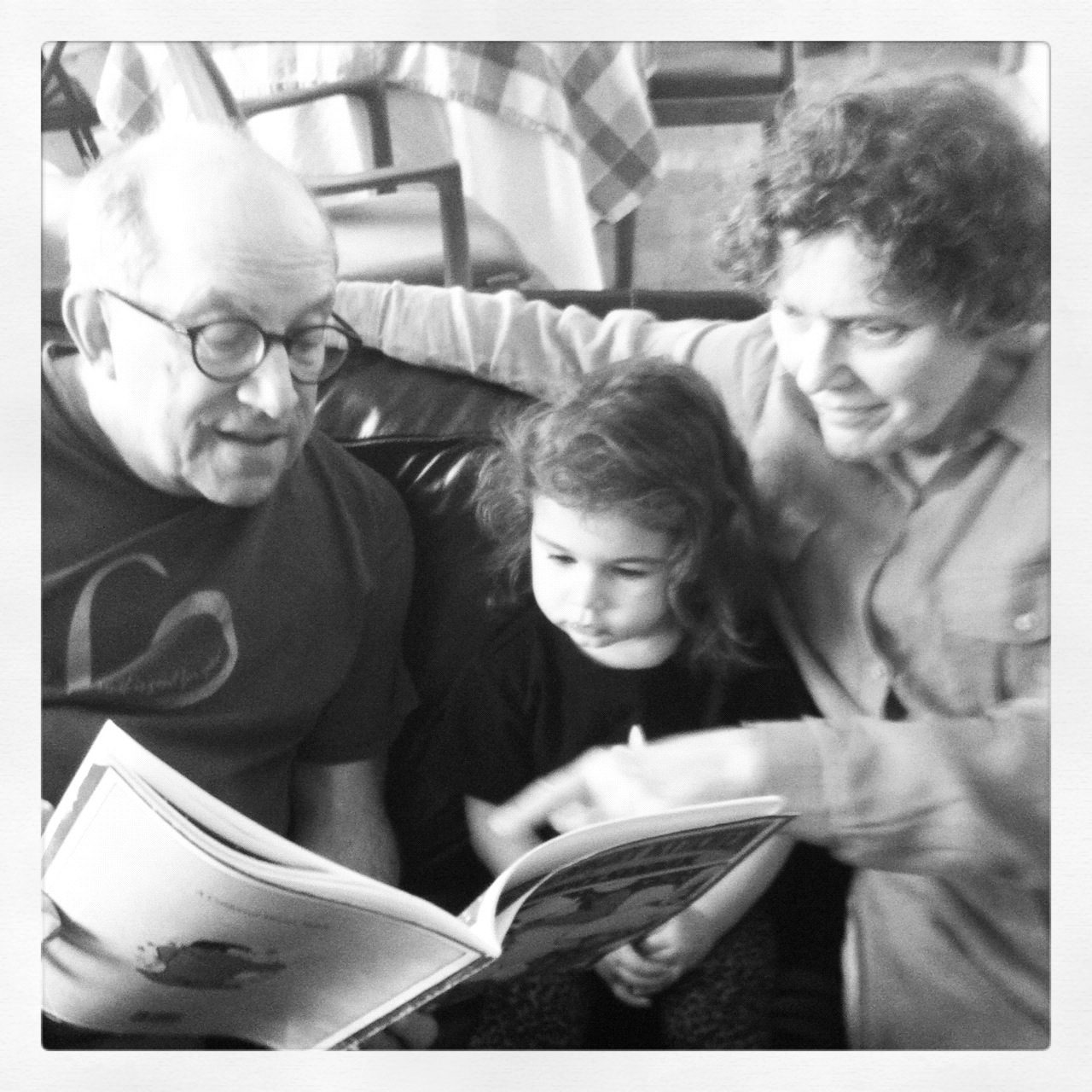 David and a woman reading a picture book with a young girl, in black and white
