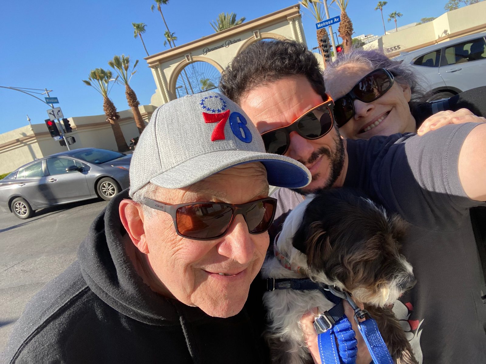 David in a 76ers cap taking a selfie with a man and a woman and a small dog in front of the Paramount Pictures gate