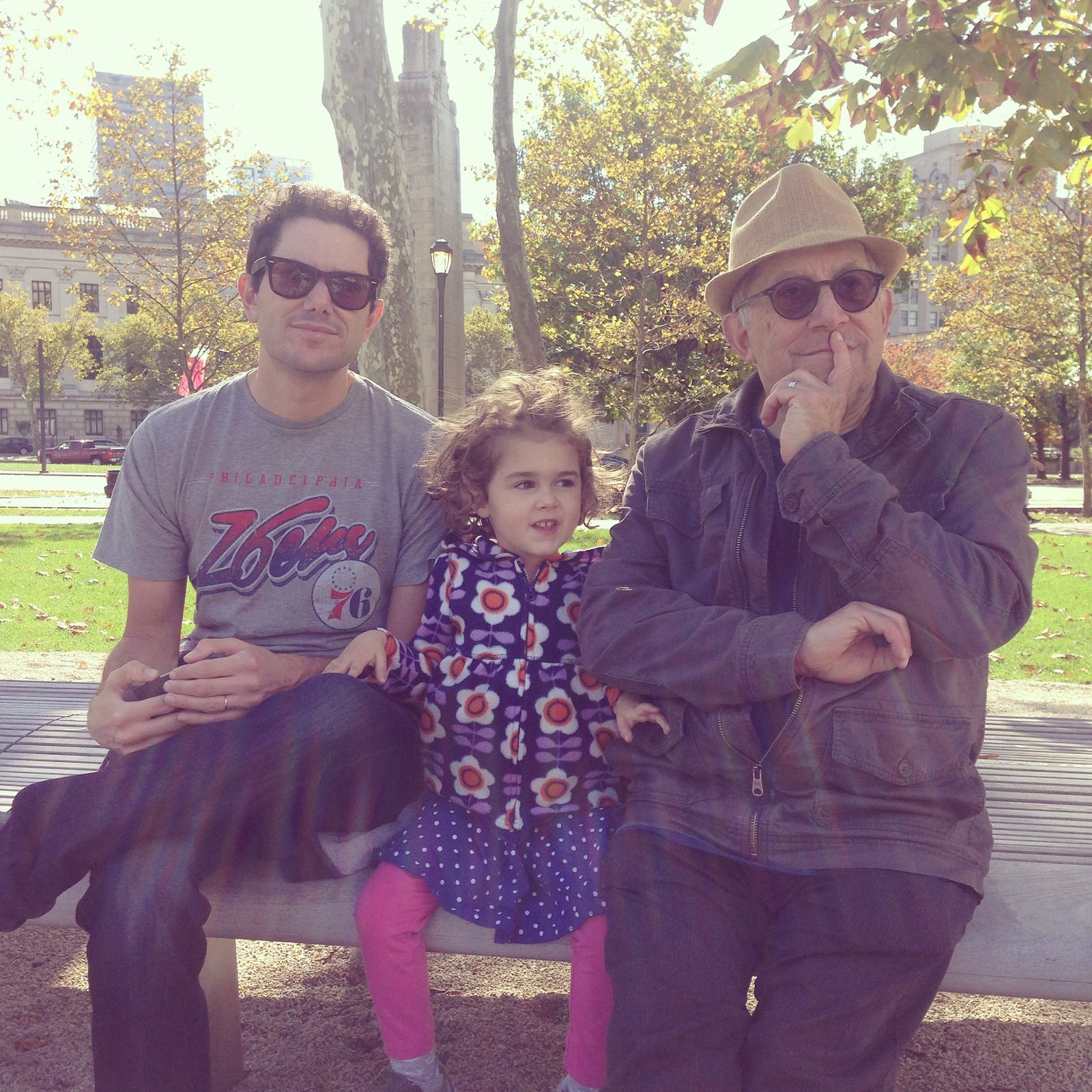 David in a straw hat on a park bench beside a man and a young girl in a flowered jacket