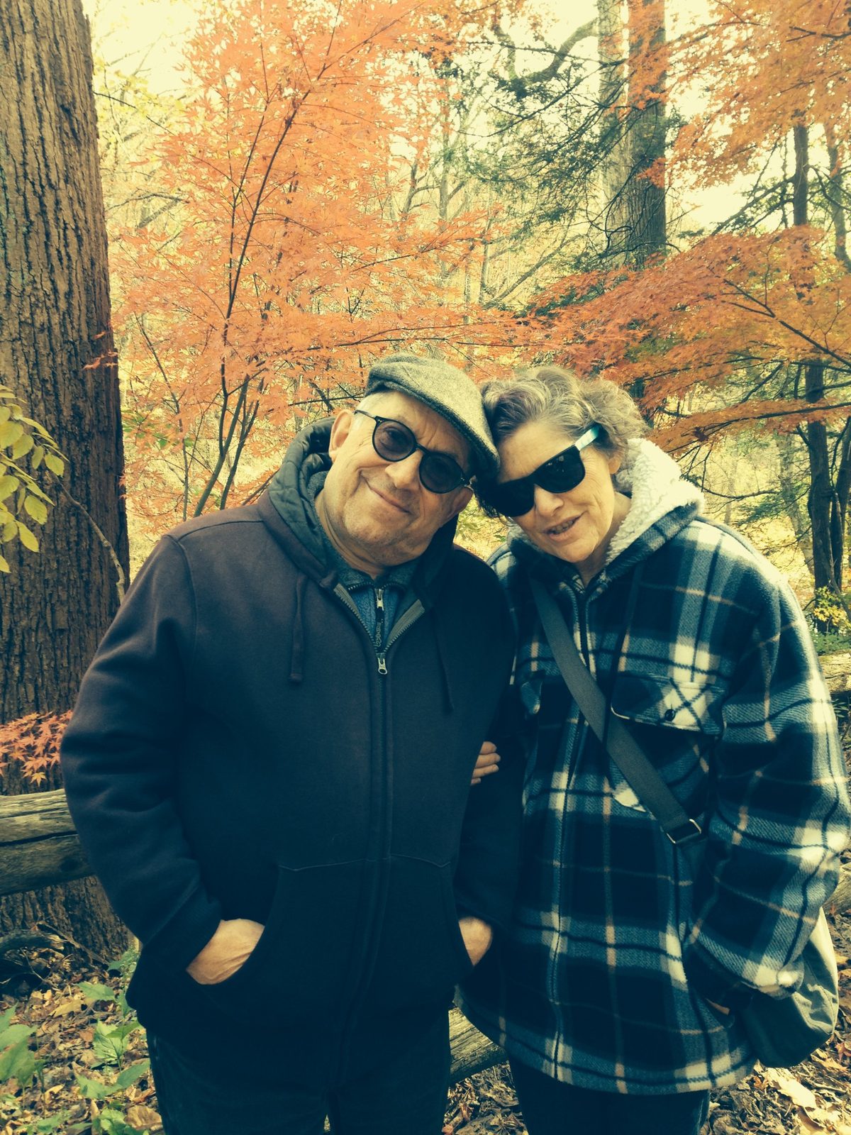 David in a flat cap and a woman leaning their heads together in front of orange autumn leaves