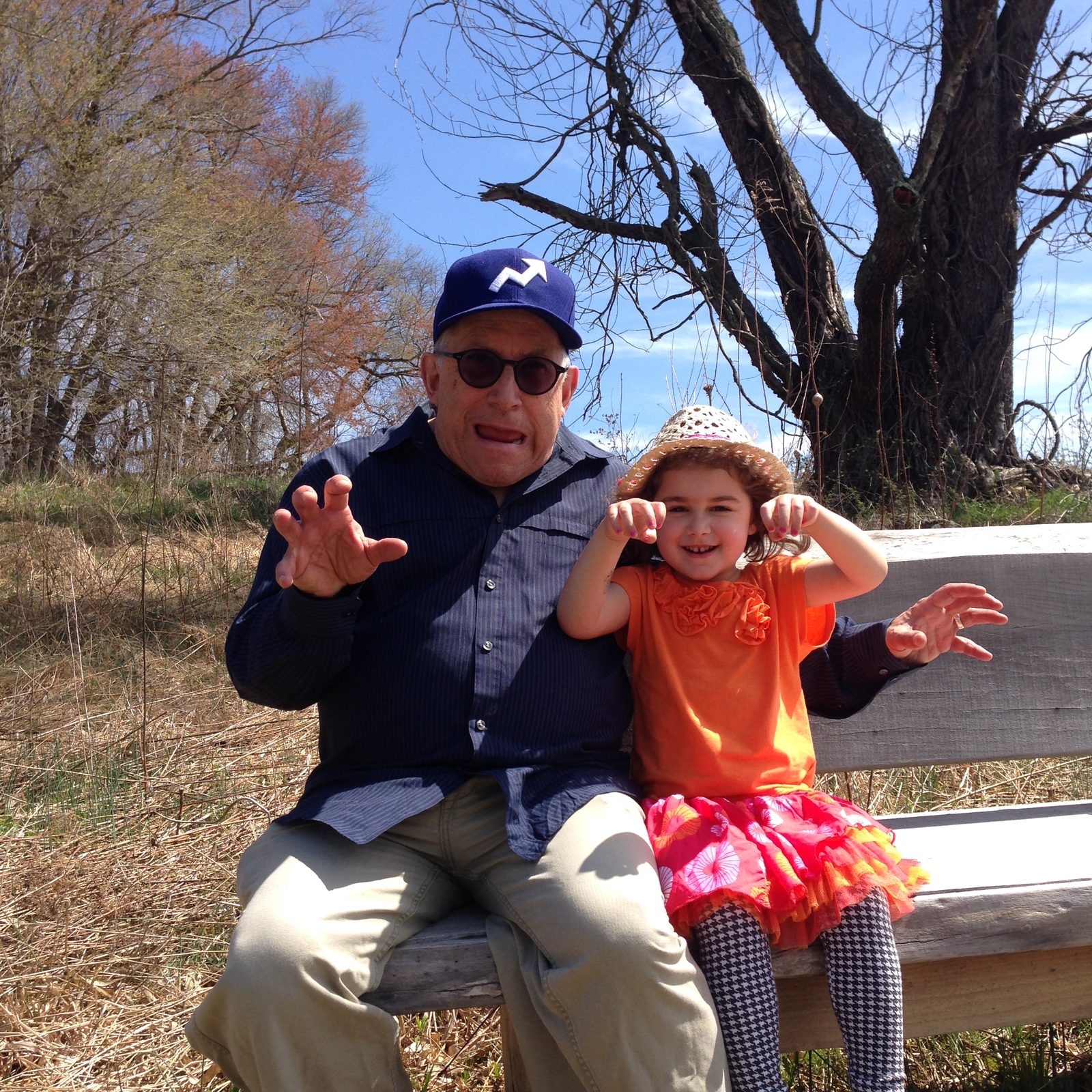 David in a blue cap on a bench with a young girl, both holding up their hands like claws