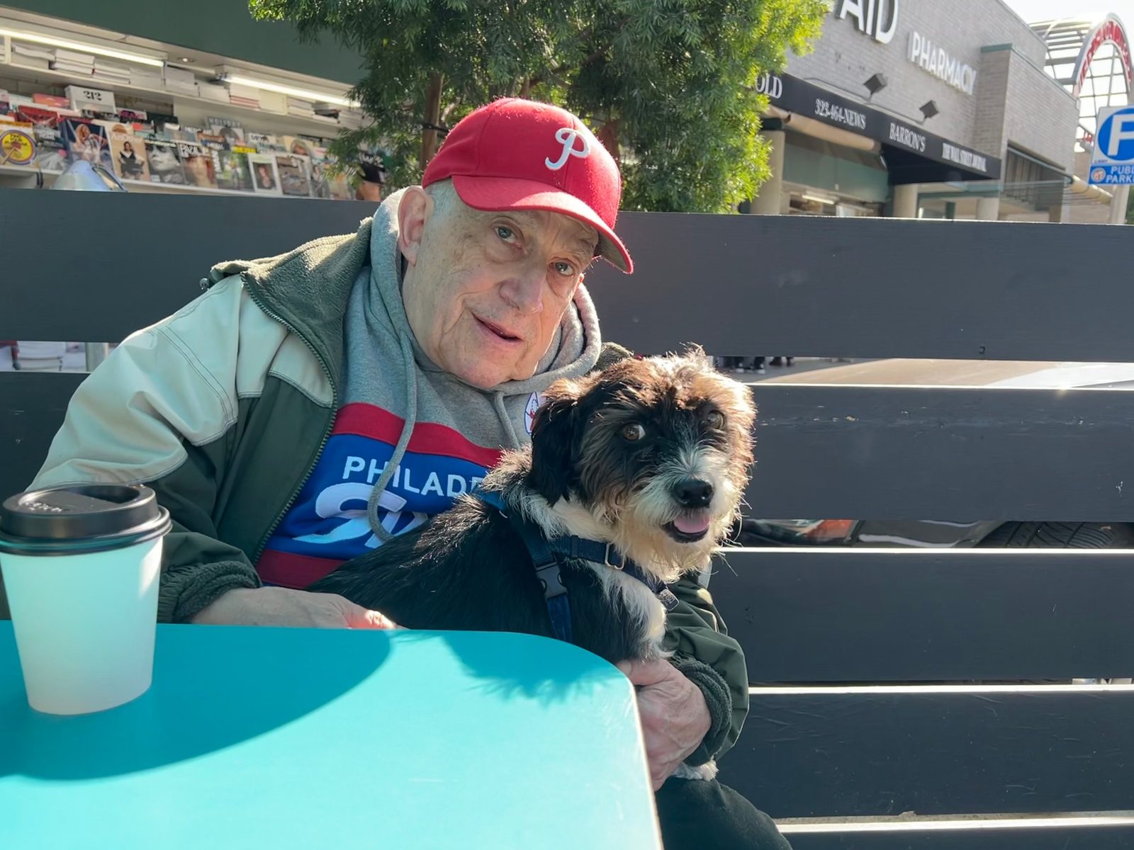 David in a Phillies cap holding a small dog at an outdoor cafe table