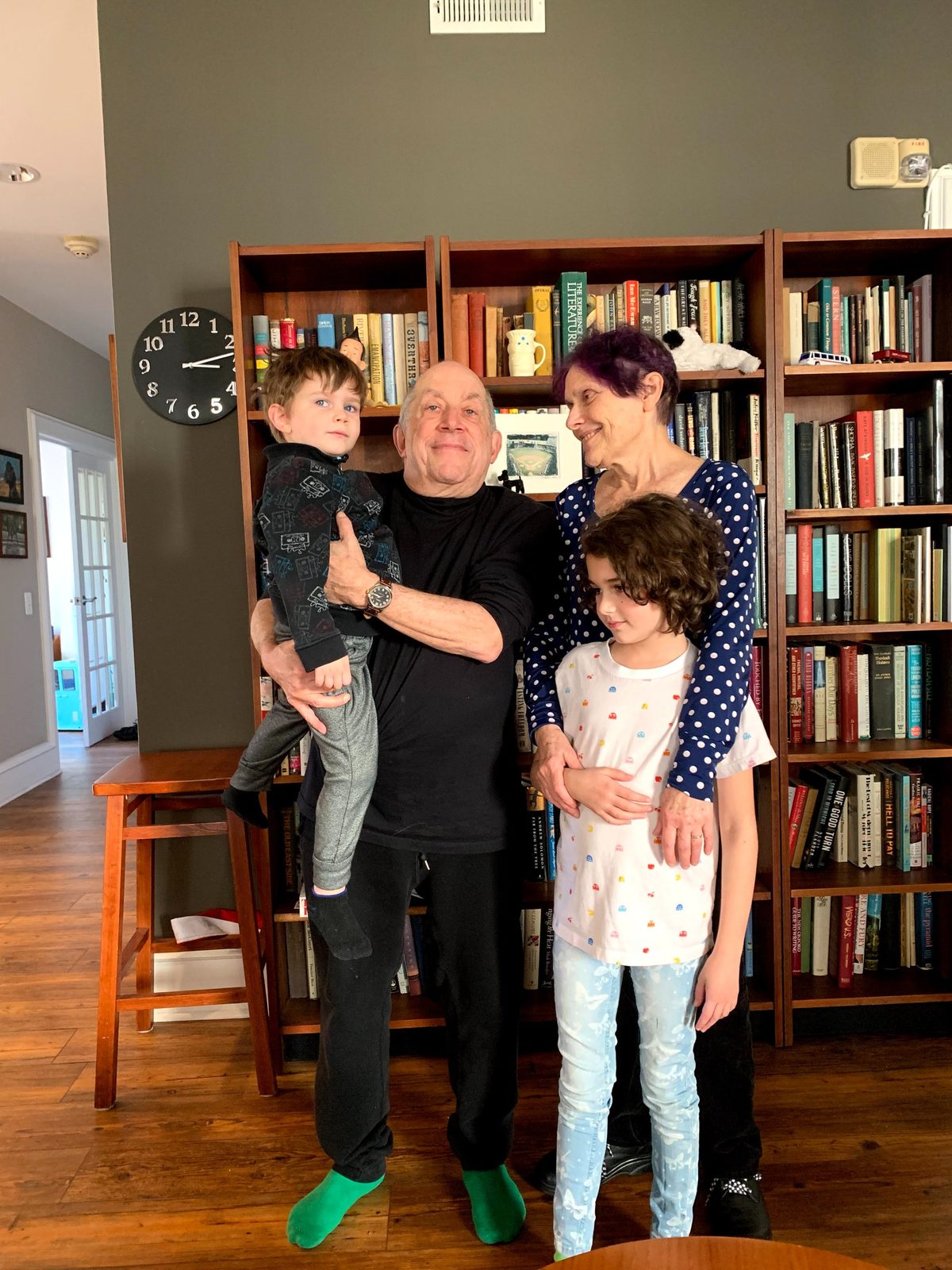 David holding a young boy while a woman and a girl stand beside him in front of a bookshelf