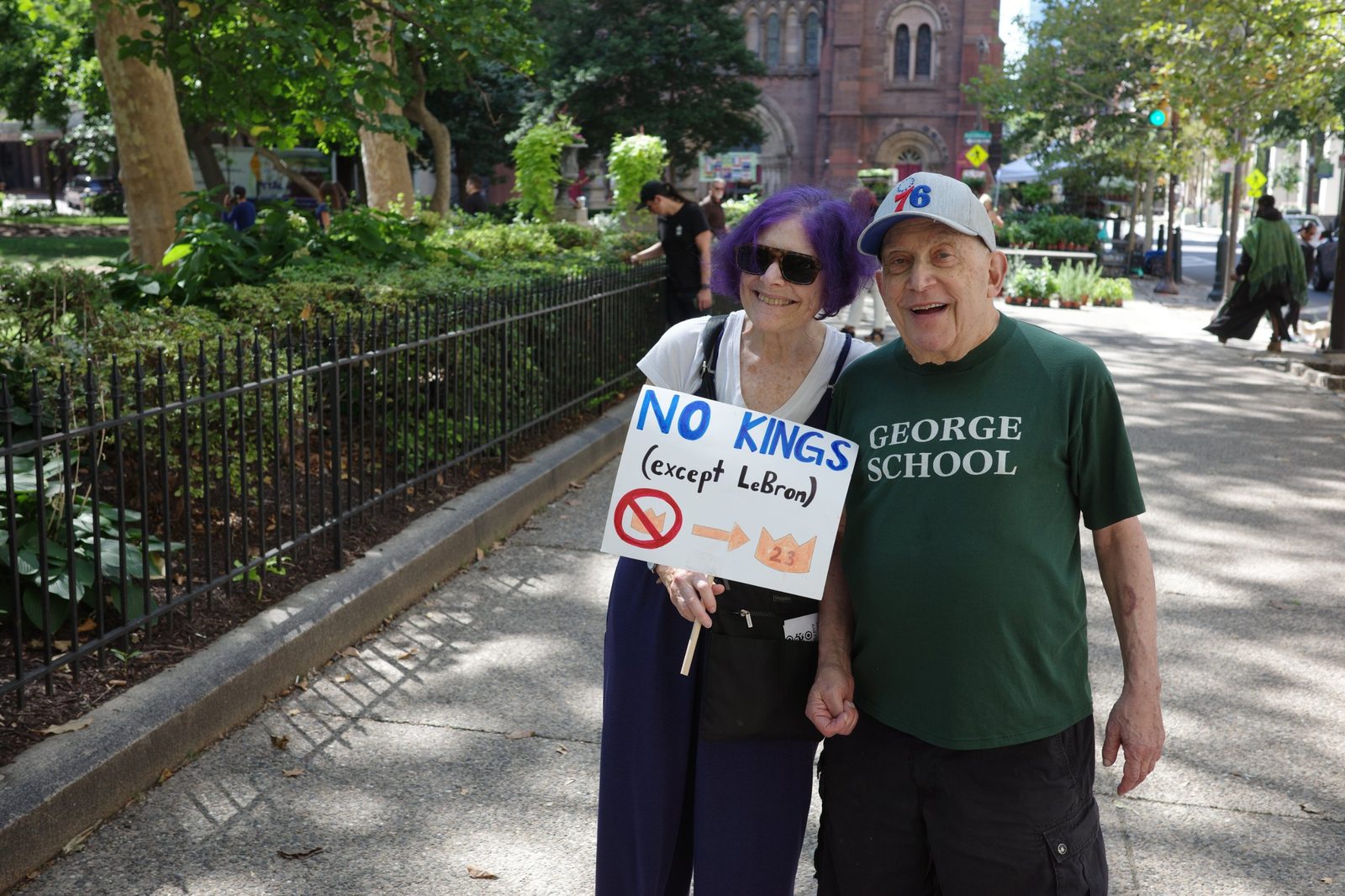 David and a woman with purple hair holding a No Kings sign in a park