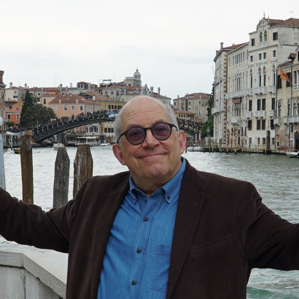 David Greenwald smiling with his arms open wide beside a canal in Venice
